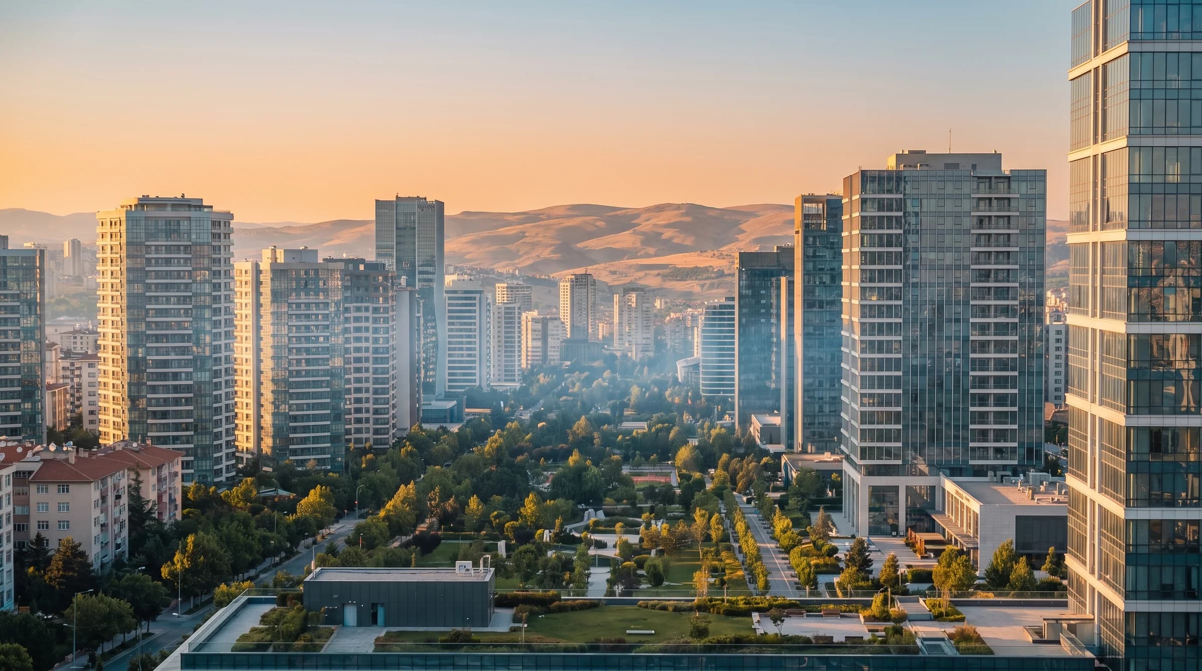 Gün batımında Ankara: modern cam kuleler, ağaçlı bir bulvar ve arkada bozkır tepeleri.